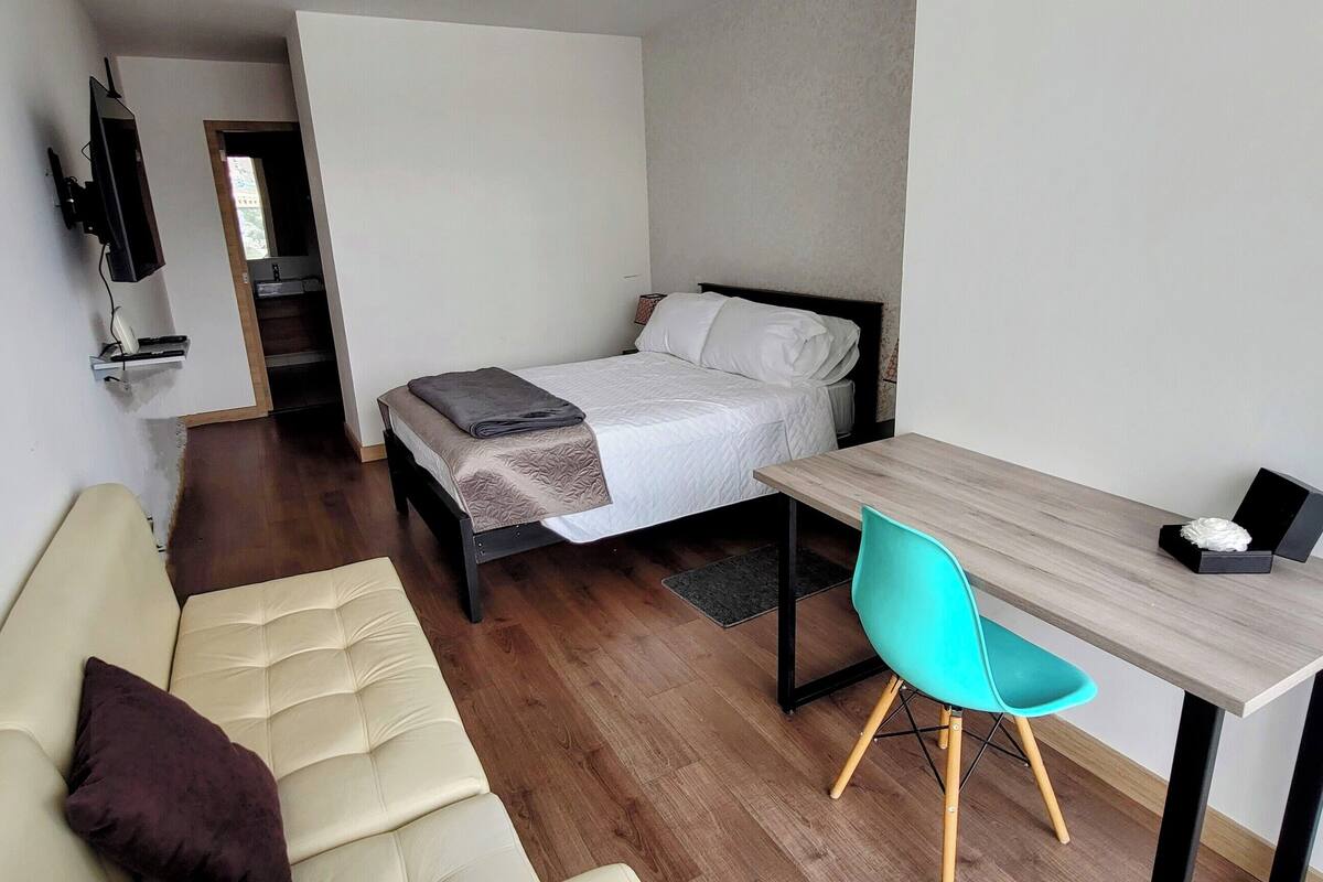 Ein gemütliches Hotelzimmer mit einem Bett, einem kleinen Schreibtisch mit Stuhl, einer Couch und einem an der Wand montierten Fernseher.