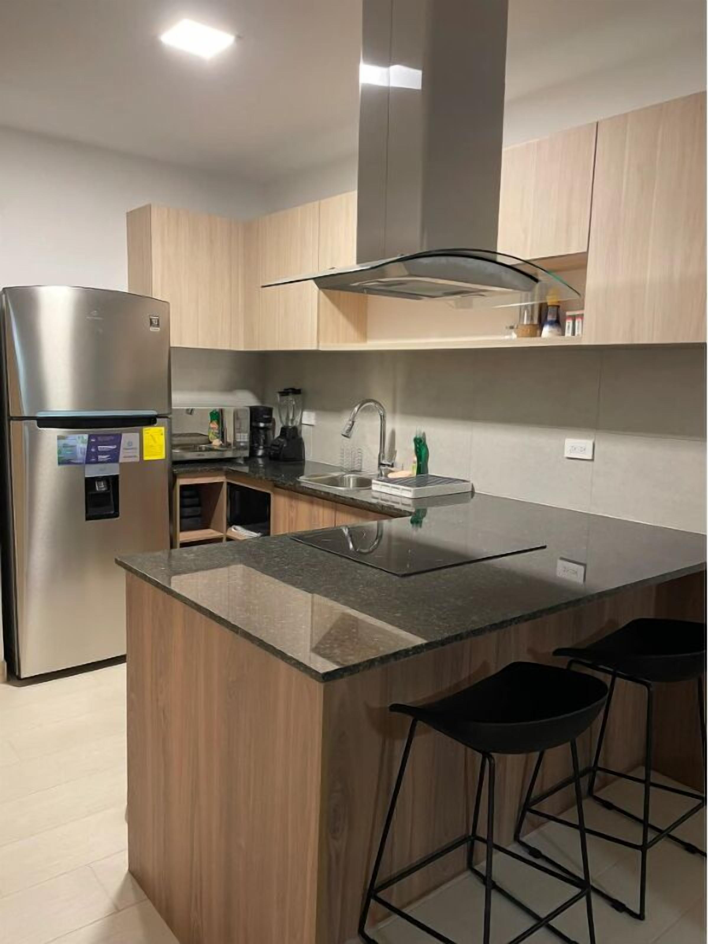 A modern kitchen with a stainless steel refrigerator, a built-in oven, a sink, and a bar area with stools.