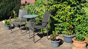 An outdoor seating area with wicker chairs and a glass table, surrounded by potted plants and a brick patio. - Apartment 'Ferienwohnung Bleichen 14' with Shared Pool, Shared Garden and Wi-Fi (Stralsund)