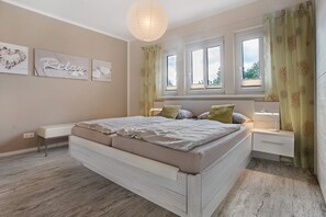 A bedroom with a bed, bedside tables, a bench, and a window with curtains. - Apartment 'Ferienwohnung Bleichen' with Private Pool, Shared Garden and Wi-Fi (Stralsund)
