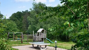 Een speeltuin met een glijbaan en schommels, omringd door bomen en een picknicktafel.