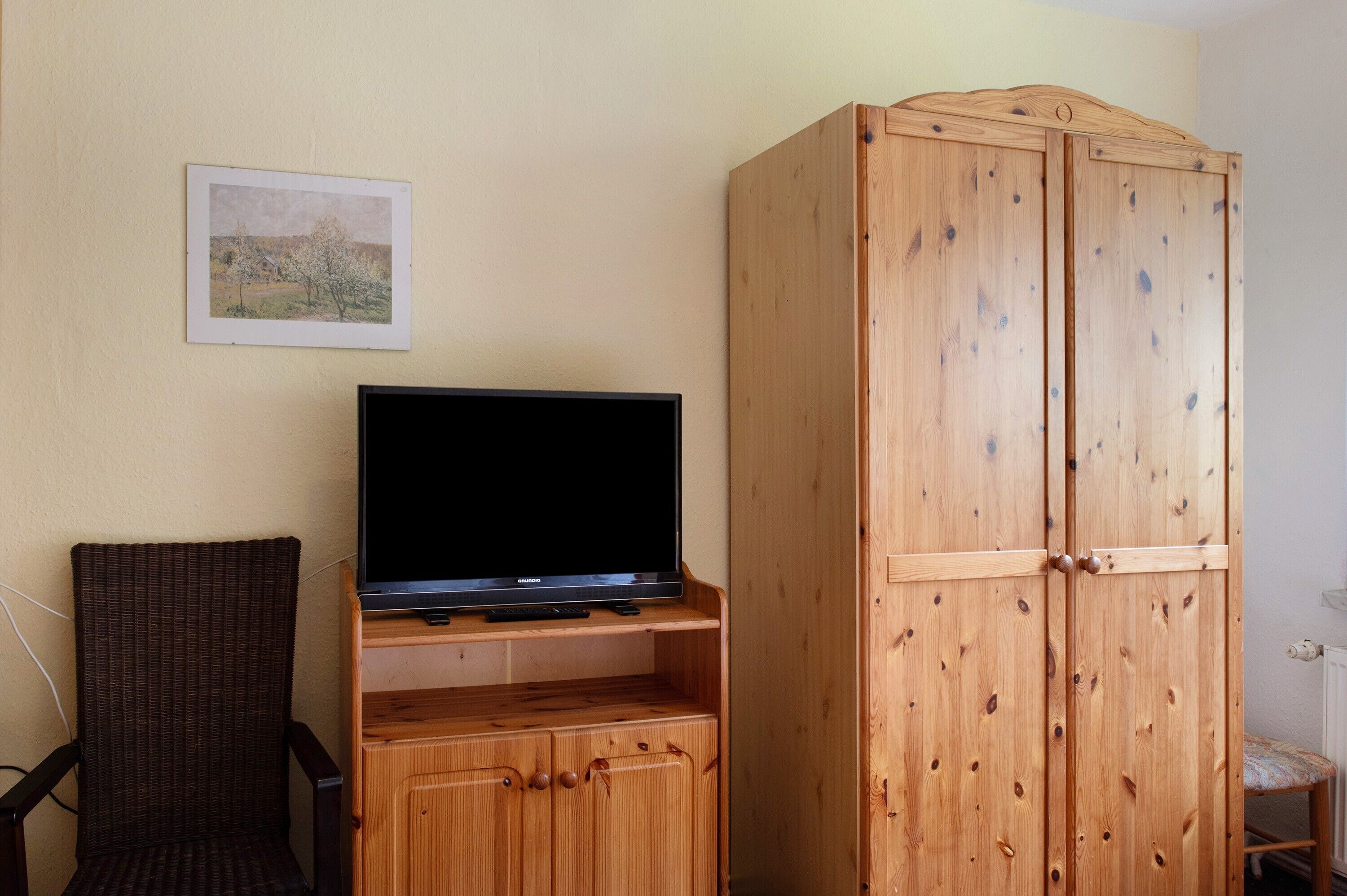 A room with a television on a wooden stand, a wicker chair, and a wooden wardrobe.