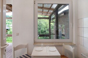 Ein Zimmer mit Fenster, Tisch mit zwei Tellern und Gläsern sowie einem Stuhl.