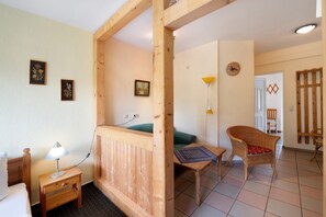 A room with a bed, a small table with a lamp, a wicker chair, and a wooden partition.