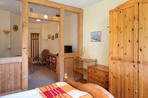 A wooden room with a bed, a wooden wardrobe, a television, and a desk with a chair.