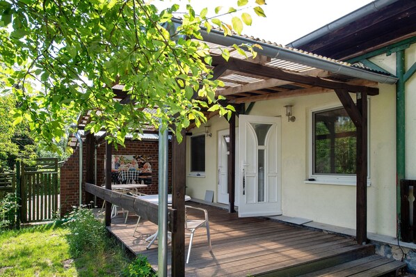 A covered outdoor patio with a wooden deck, a brick wall, and a white door.