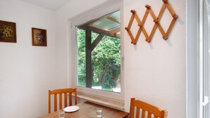 Un comedor con una mesa de madera, dos sillas, una ventana con vistas a zonas verdes y dos cuadros en la pared.