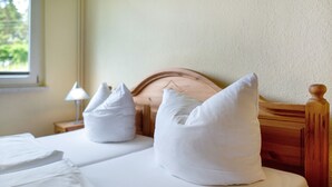 Una cama bien tendida con ropa de cama y almohadas blancas, un cabecero de madera y una lámpara de noche.