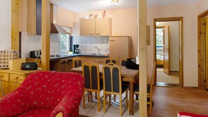 Une cuisine de taille réduite avec des meubles de rangement en bois, une table à manger avec des chaises et un fauteuil rouge.
