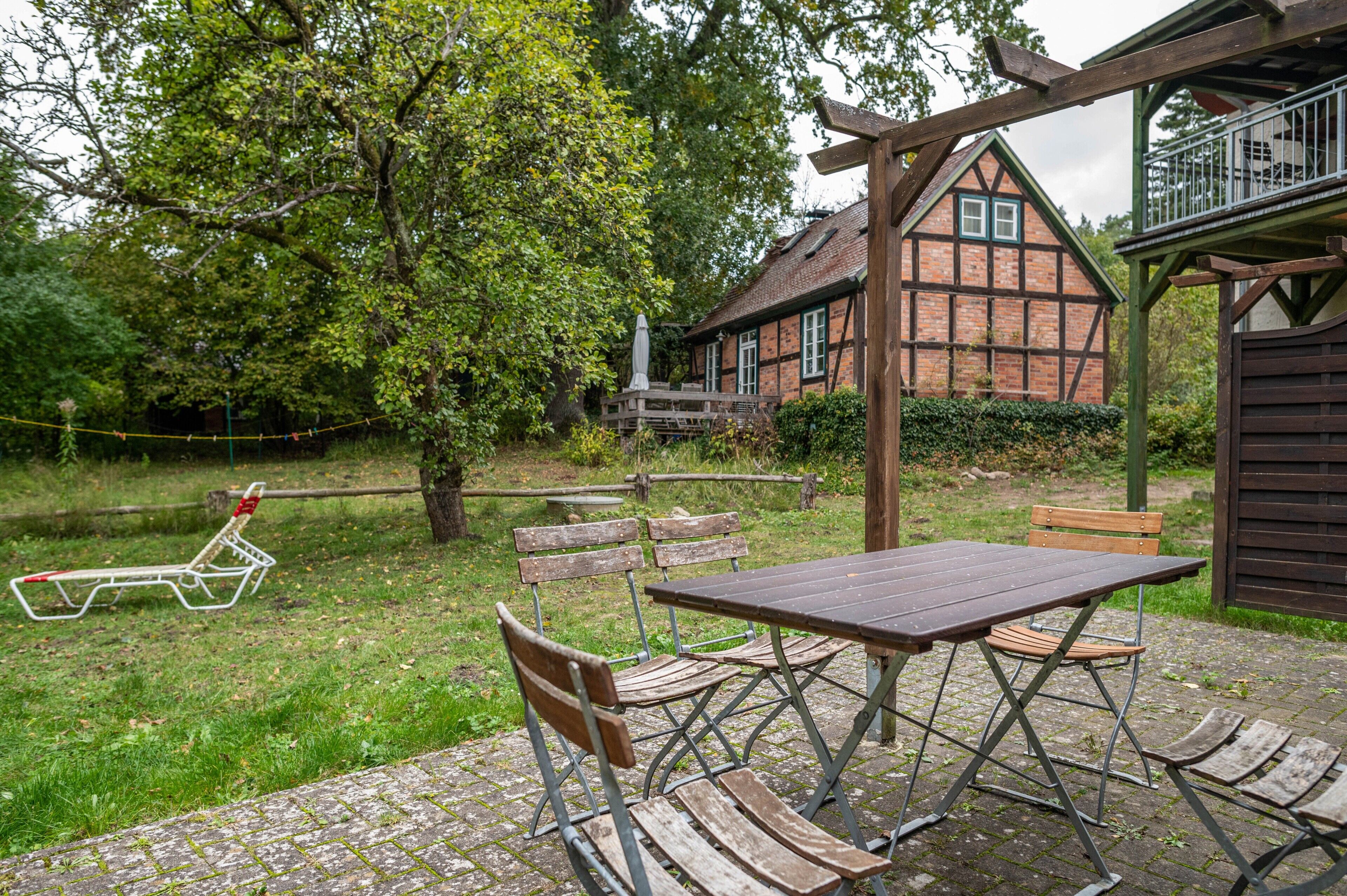 A rustic outdoor seating area with a wooden table and benches, a picnic table, and a traditional house in the background.