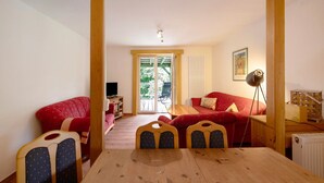 Une pièce chaleureuse avec une table en bois, deux canapés rouges et un petit balcon avec une chaise.