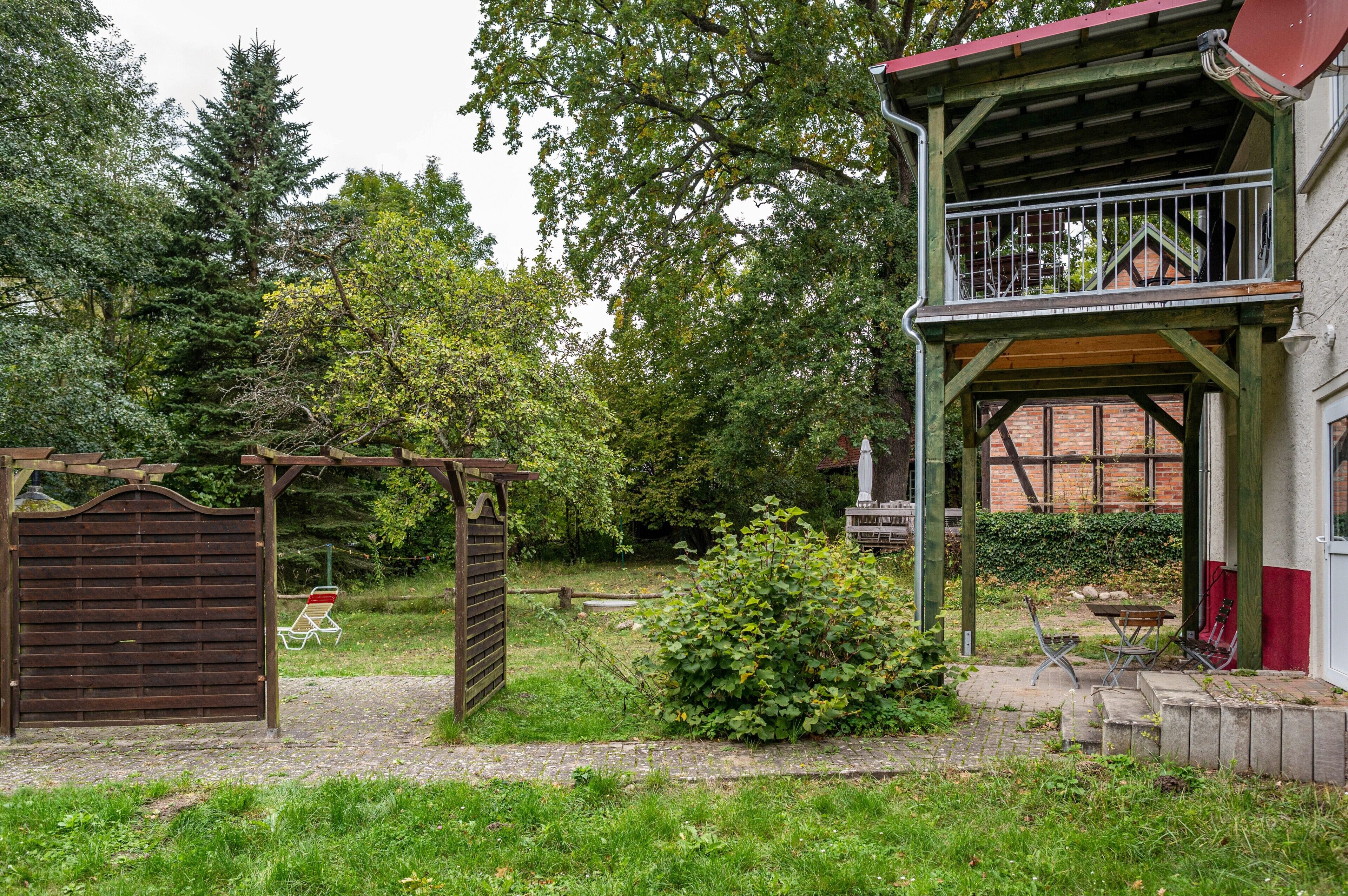 A wooden structure with a balcony, a brick wall, and a garden area with a bench and a statue.
