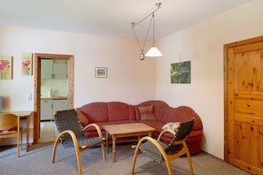 Un salon comprenant un canapé, deux fauteuils, une table en bois, un luminaire suspendu et une porte en bois.