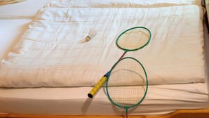 Una cama con ropa de cama blanca, un volante de bádminton y dos raquetas.