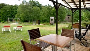 An outdoor patio with a wooden table and chairs, a swing set, and a small shed in a grassy area with trees in the background. - Holiday home 'Rethra Nord' with private terrace and WLAN (Feldberger Seenlandschaft)