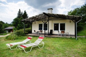Ein überdachter Außenbereich mit zwei Liegestühlen, einem Tisch und Stühlen sowie ein Gebäude mit Fenstern und Schornstein.