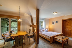 A room with a wooden table, chairs, a bed, a small table, and a window.