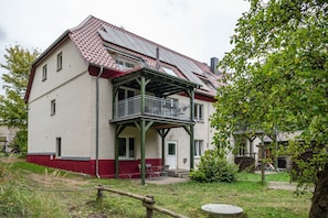 A two-story building with a balcony, a door, and a small outdoor seating area.