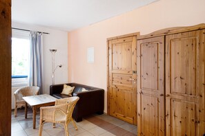 Ein Zimmer mit einer Couch, zwei Korbstühlen, einem Tisch, einer Stehlampe und Holzschränken.