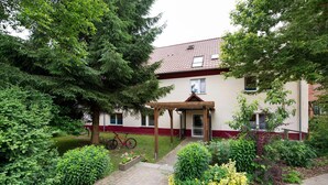 Ein Gebäude mit rotem Ziegeldach, einer überdachten Eingangspartei und einem Garten mit verschiedenen Pflanzen sowie einem Fahrrad.