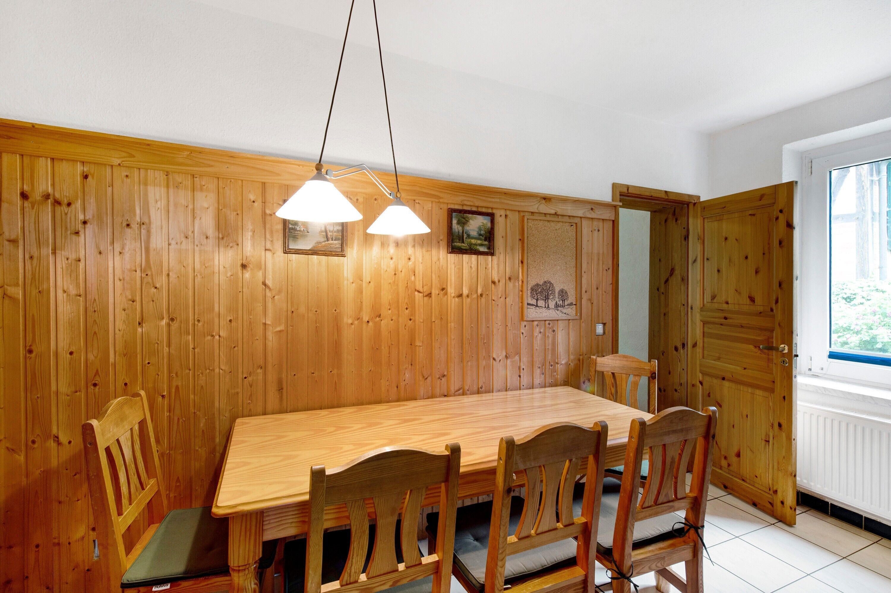 Comedor con paneles de madera, una larga mesa y sillas, iluminación colgante y un ventanal con vistas.