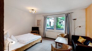 Ein Zimmer mit einem Bett, einem kleinen Tisch, einer Couch, einem Fernseher und einem Fenster mit Vorhängen.