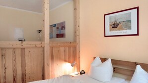 A bedroom with a wooden headboard, a framed artwork, a bedside lamp, and a bed with pillows.