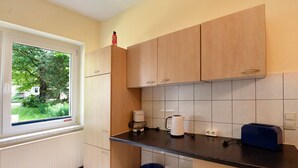 A kitchen with wooden cabinets, a window with a view of greenery, a coffee maker, a kettle, and a toaster.