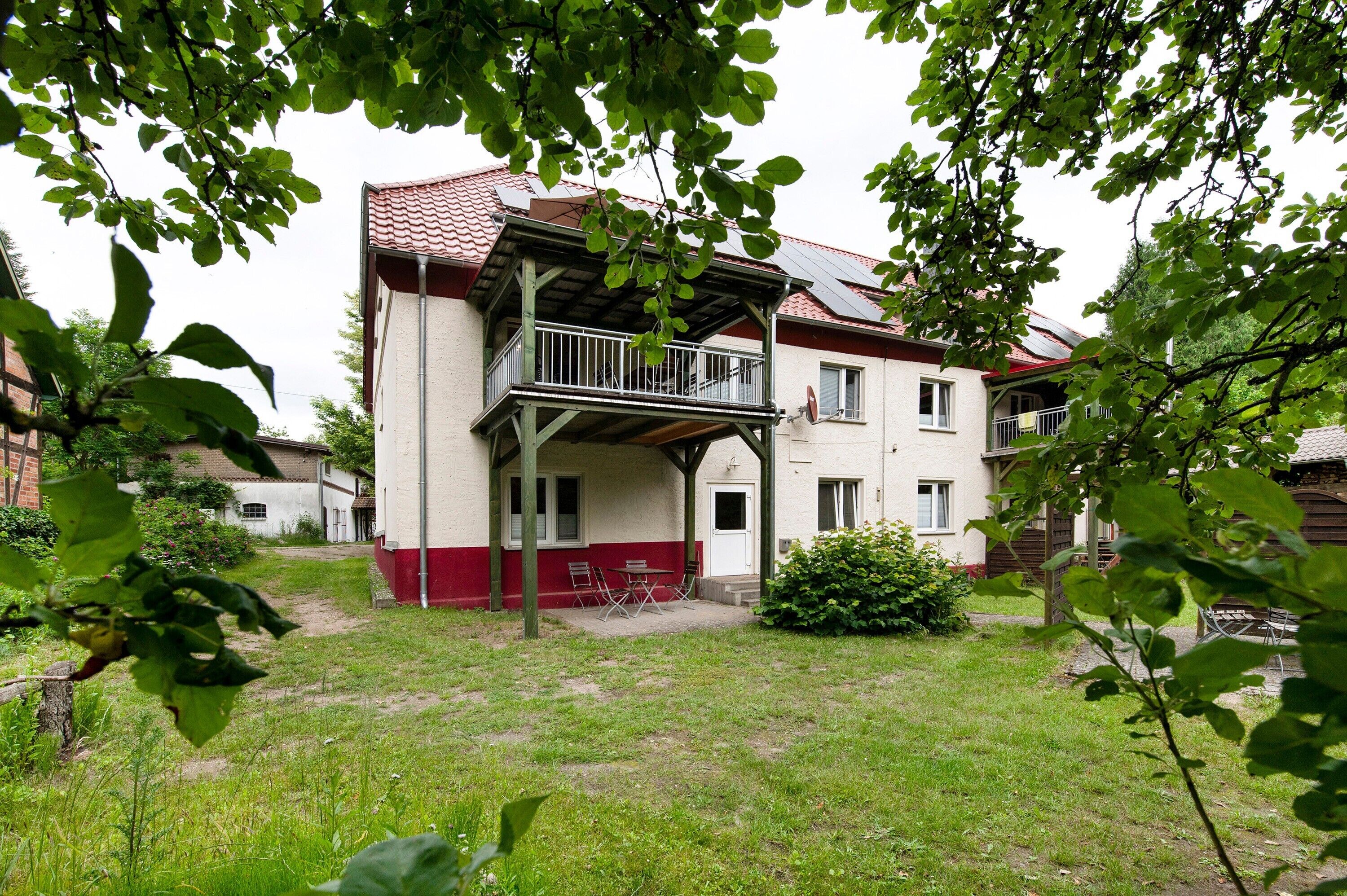Ein zweistöckiges Gebäude mit Balkon, überdachter Terrasse und einem kleinen Garten.