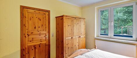 A bedroom with a bed, wooden wardrobe, and a window with a view of greenery.