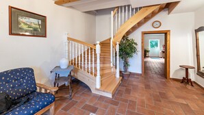 Un escalier avec des rampes en bois, un canapé bleu à motifs, une petite table recouverte d’une nappe à carreaux et une plante en pot.