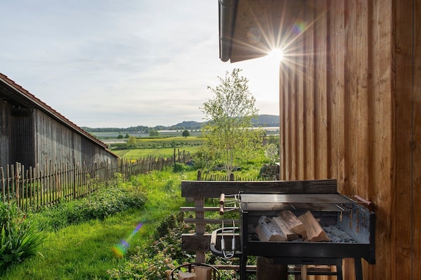 A rustic wooden building with a view of a green landscape, a wooden fence, and a barbecue grill.