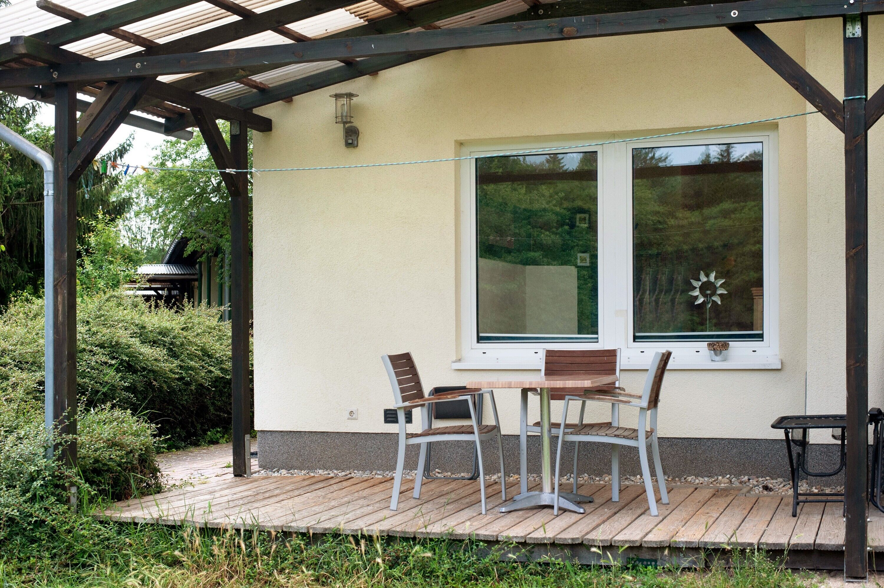 Ein überdachter Patio-Bereich mit Tisch und Stühlen, ein Fenster mit Sonnendekoration und ein Grill im Hintergrund.