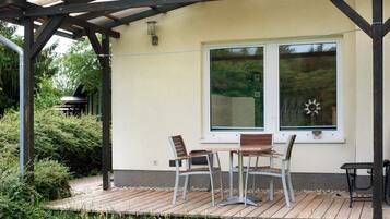 Ein überdachter Patio-Bereich mit Tisch und Stühlen, ein Fenster mit Sonnendekoration und ein Grill im Hintergrund.