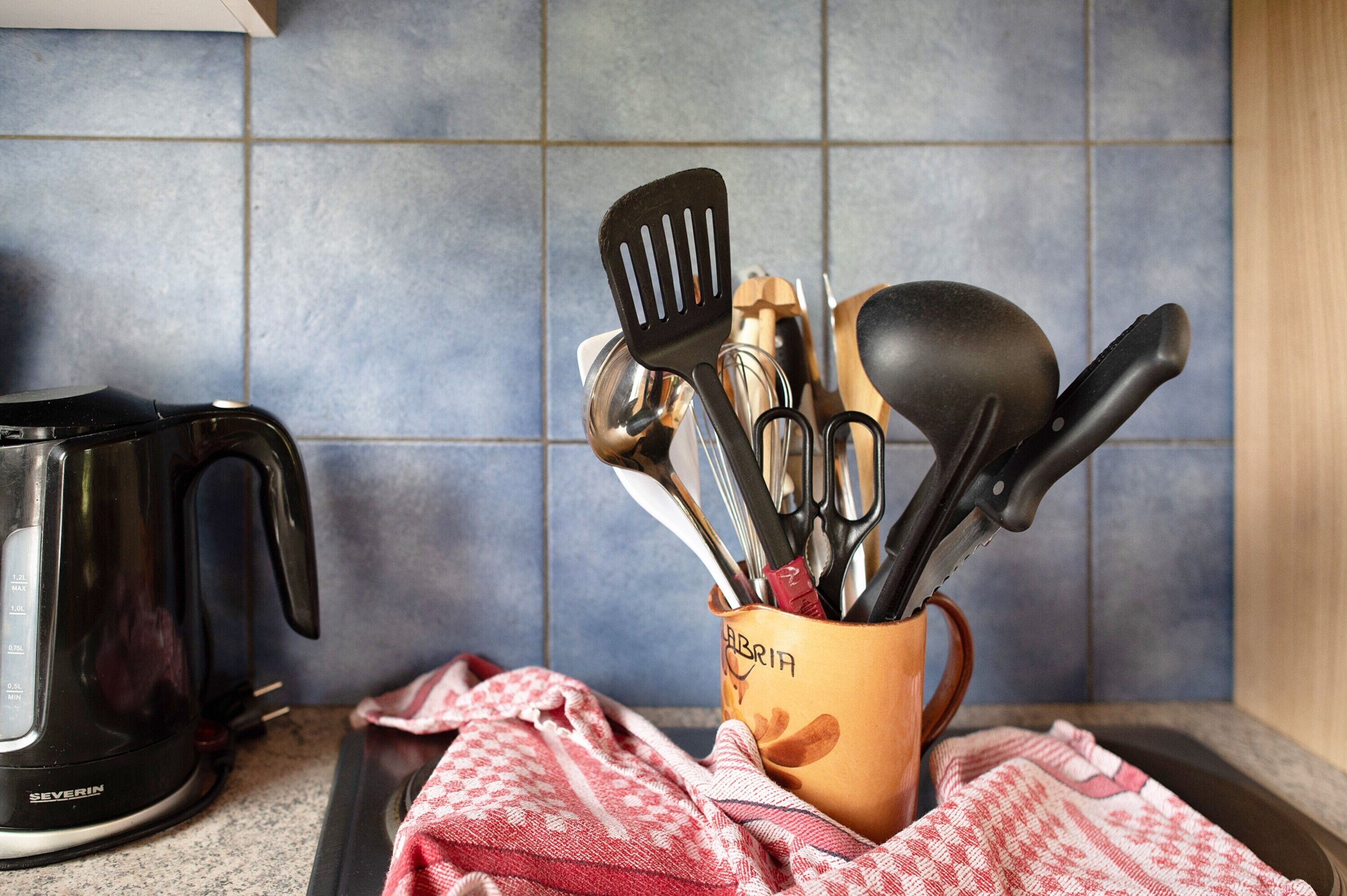 A kitchen counter with a coffee maker, a utensil holder, and a red and white checkered cloth.