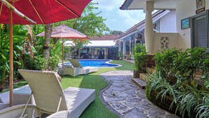 A pool area with artificial turf, stone pathway, and outdoor furniture. - Attara Heritage Senggigi (Senggigi)