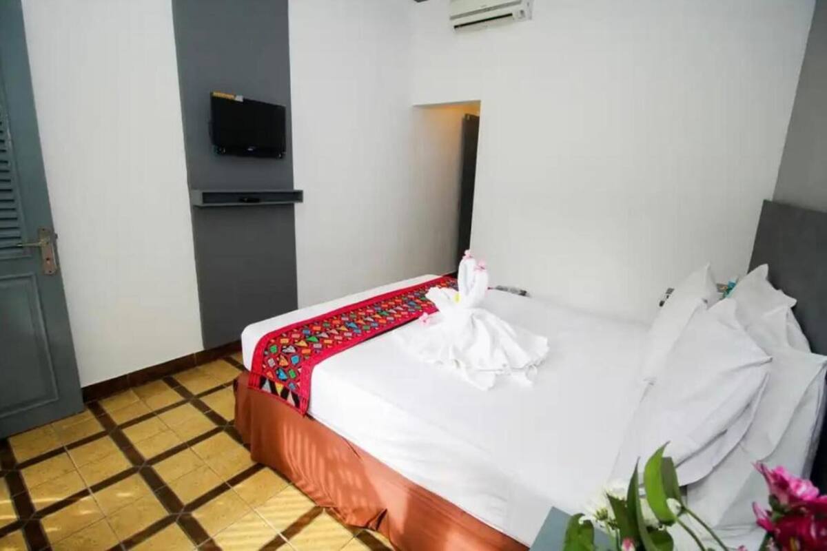 A hotel room with a bed, a TV mounted on the wall, and a tiled floor.