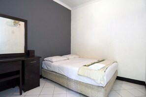 Quarto pequeno com uma cama de solteiro, escrivaninha de madeira escura e espelho.