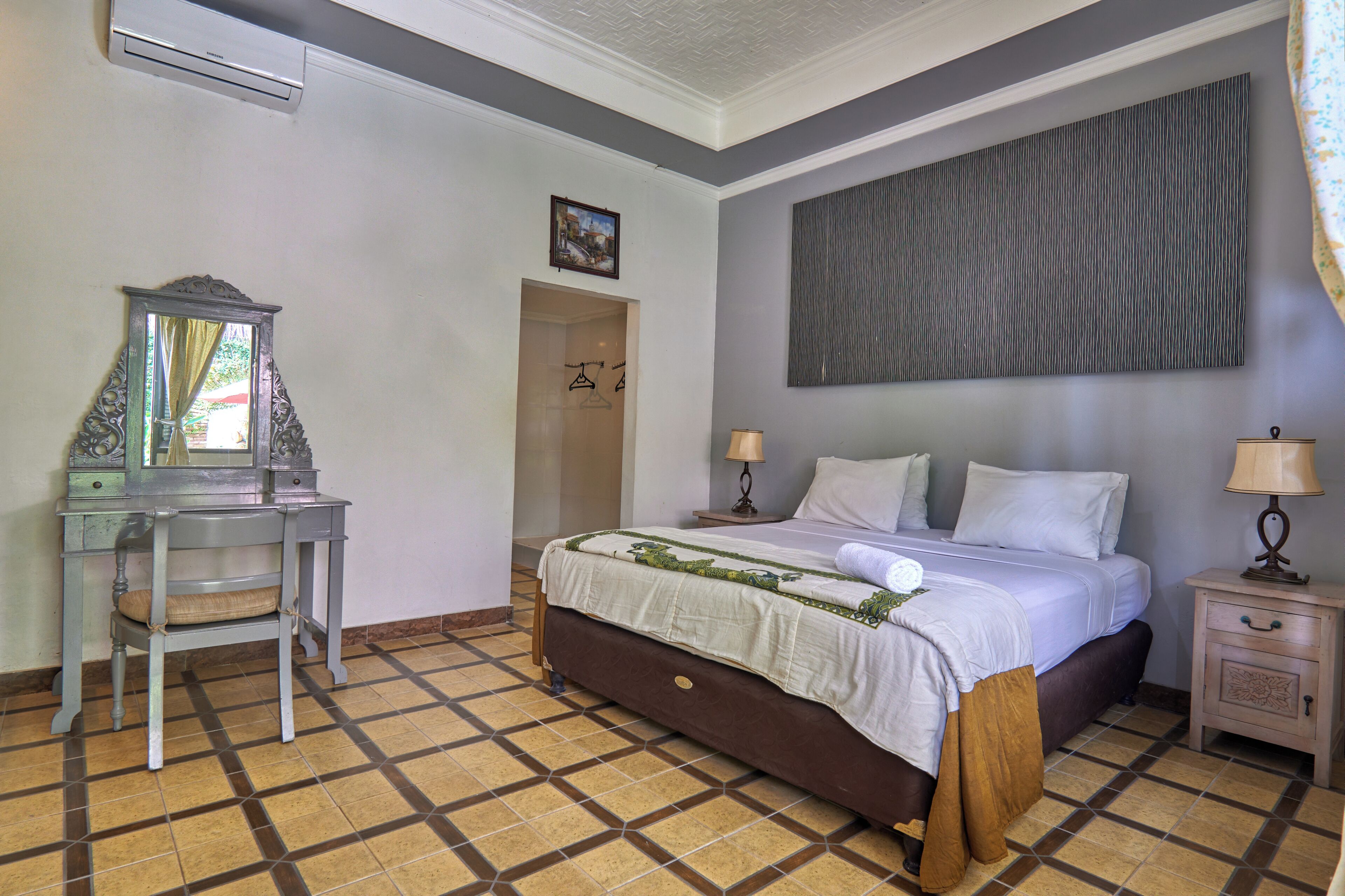 Une chambre d’hôtel avec un lit, un bureau, un miroir, un tableau et un sol à motifs.