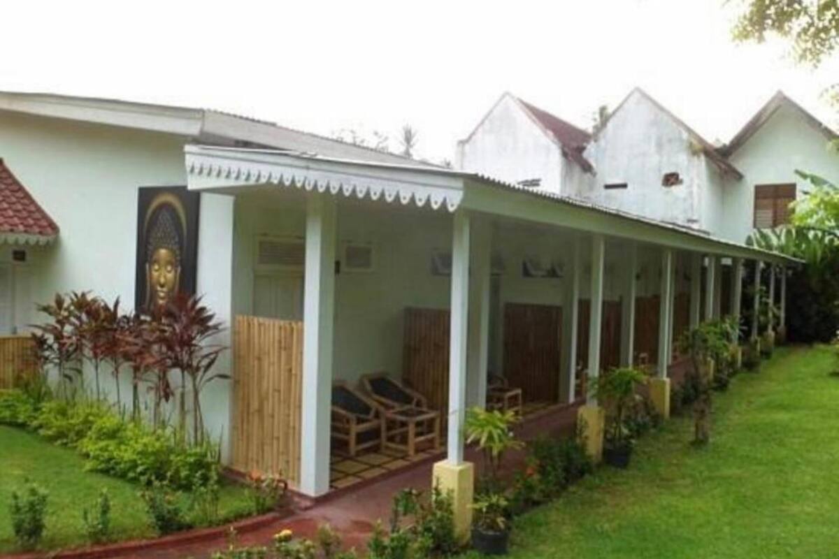 A row of single-story houses with a covered porch area, each with a wooden bench and potted plants.