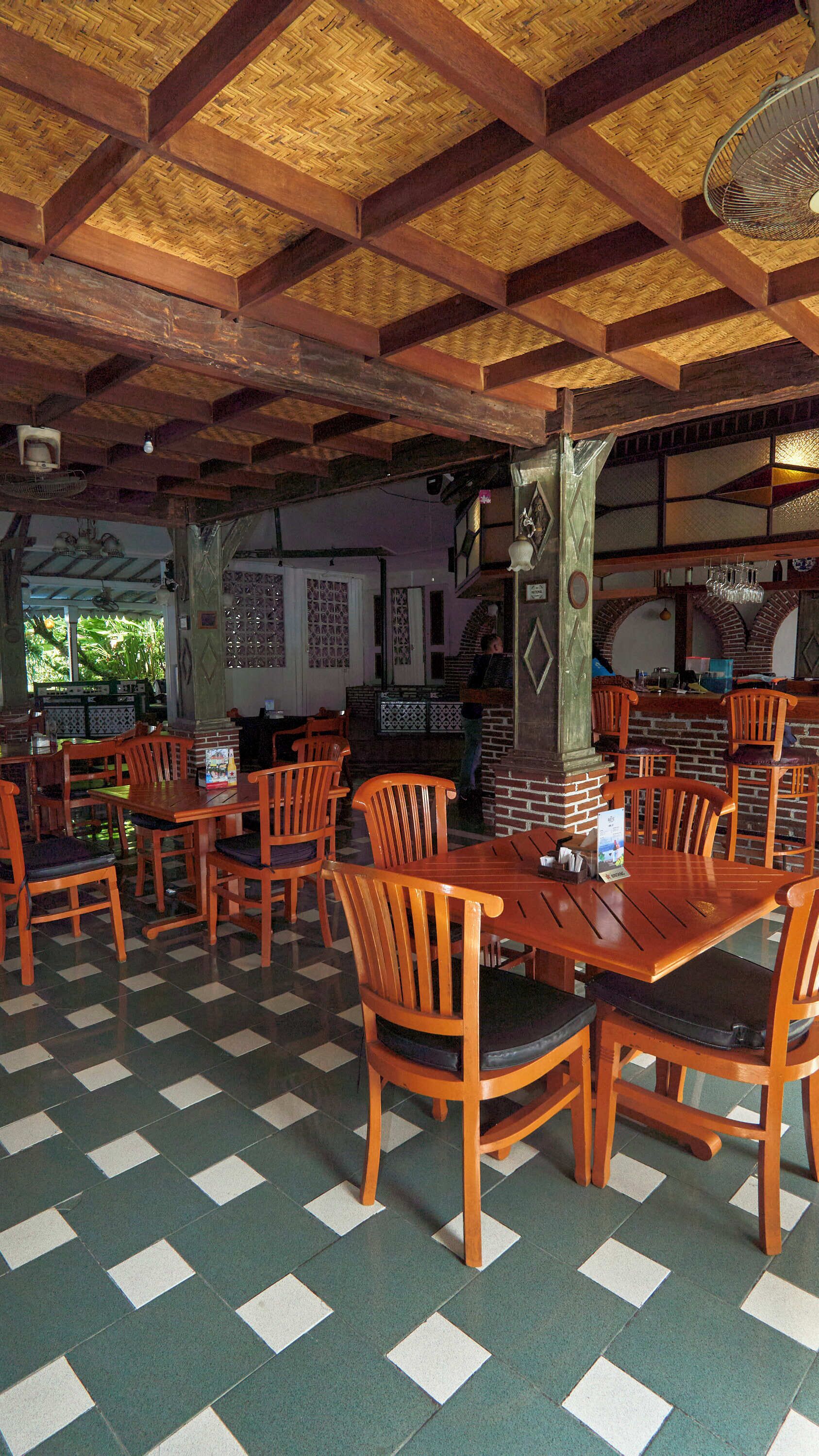 Een restaurant met houten tafels en stoelen, een betegelde vloer en een rieten dak.
