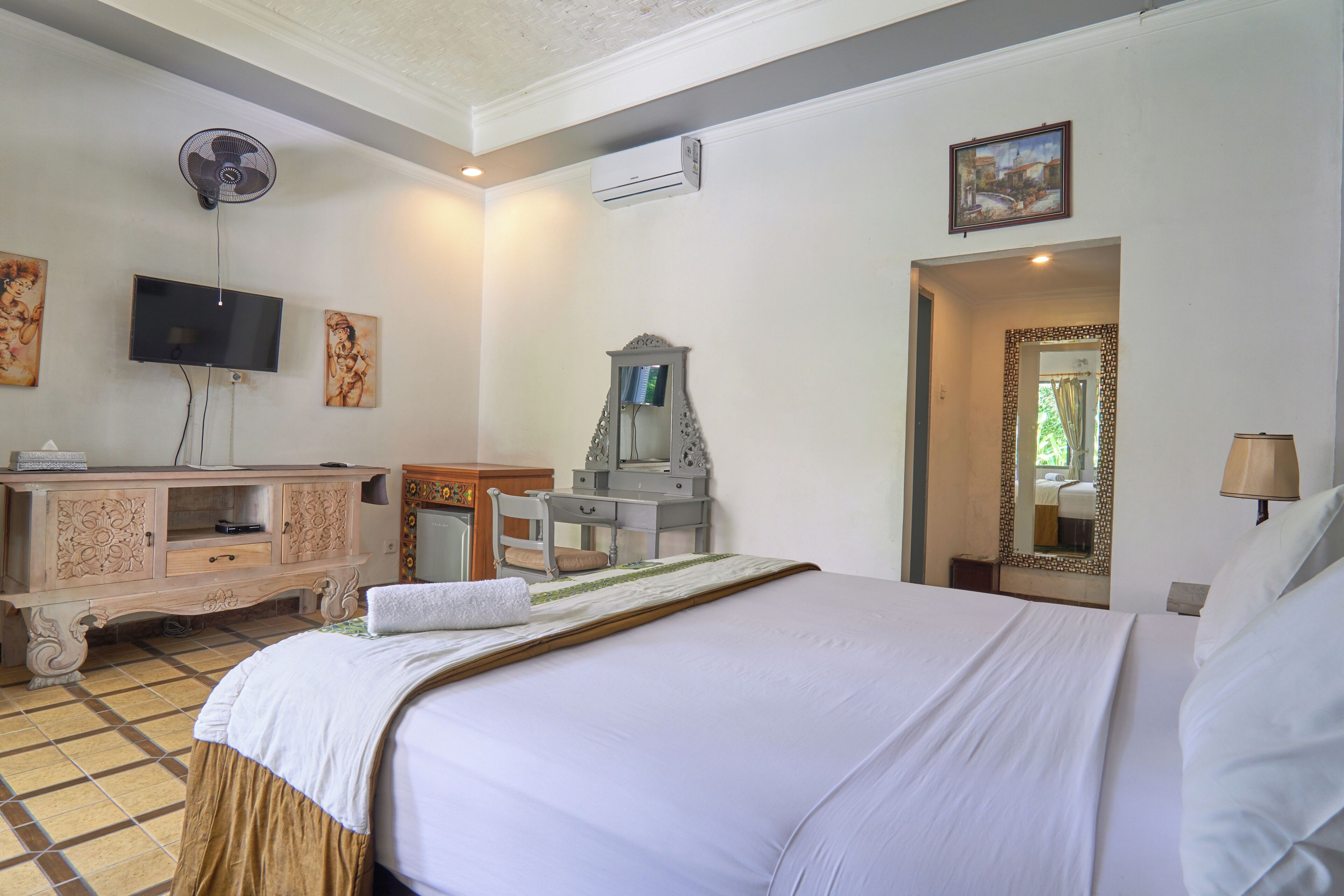 Habitación de hotel con cama, escritorio, televisor y espejo.