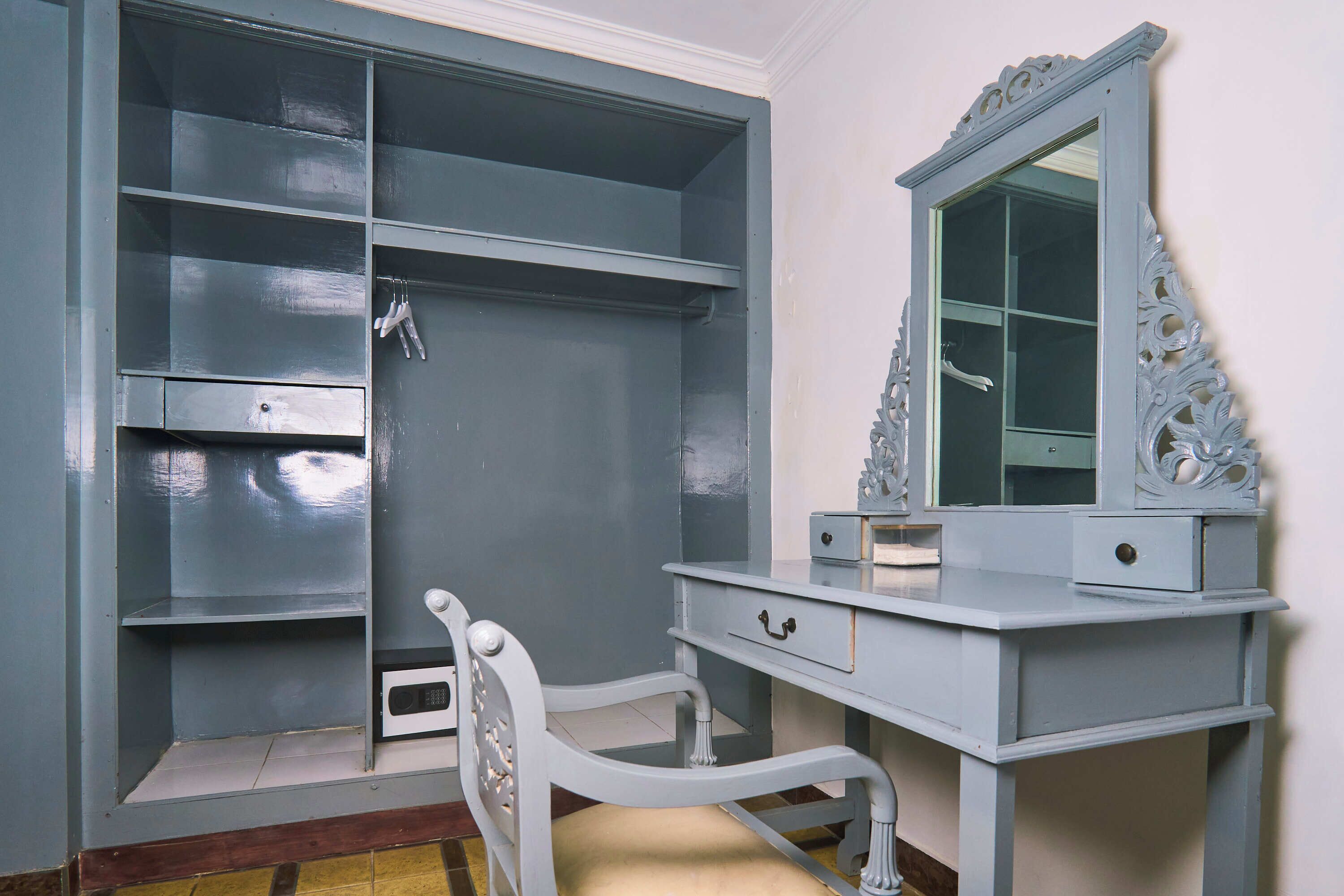 A room with a grey wardrobe, a vanity with a mirror, and a chair.