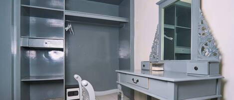 A room with a grey wardrobe, a vanity with a mirror, and a chair.