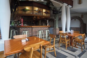 Interno di un ristorante con tavoli e sedie in legno, una zona bar con sgabelli e un muro in mattoni.