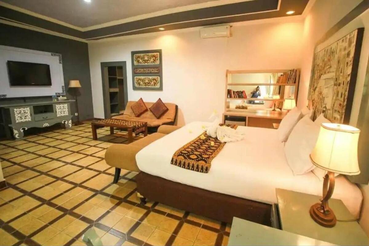 A hotel room with a large bed, a TV, a desk, and a bookshelf.