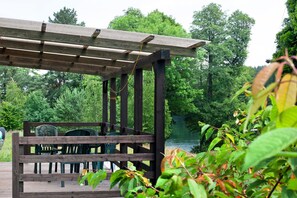 A wooden pergola with chairs and a table, overlooking a lake surrounded by trees. - Holiday Home 'Ferienhaus Utkieck' with Private Terrace, Shared Garden and Wi-Fi (Feldberger Seenlandschaft)