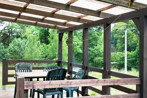 A covered outdoor area with a table and chairs, surrounded by a wooden railing, overlooking a natural landscape. - Holiday Home 'Ferienhaus Utkieck' with Private Terrace, Shared Garden and Wi-Fi (Feldberger Seenlandschaft)