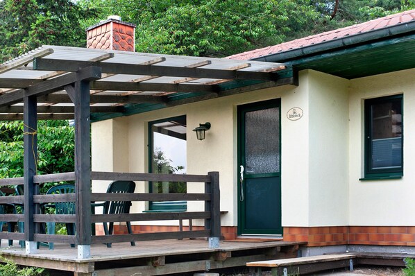 Un espace extérieur abrité, doté d’une terrasse en bois, d’un banc et d’une porte avec une pancarte.