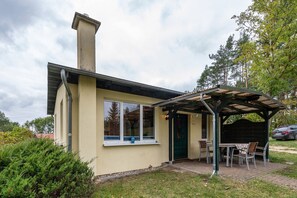 Un petit bâtiment doté d’un patio couvert, d’une cheminée et d’une fenêtre sur le rebord de laquelle se trouve un objet bleu.